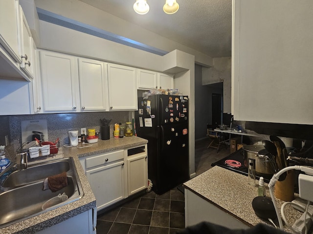 kitchen with black refrigerator, sink, a textured ceiling, white cabinets, and dark tile patterned floors