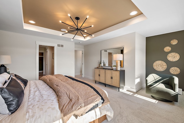 carpeted bedroom with ensuite bathroom, a tray ceiling, and a chandelier