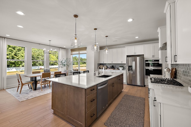 kitchen with appliances with stainless steel finishes, decorative light fixtures, white cabinetry, sink, and a center island with sink