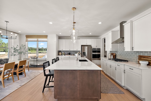 kitchen with pendant lighting, white cabinets, wall chimney range hood, stainless steel appliances, and sink