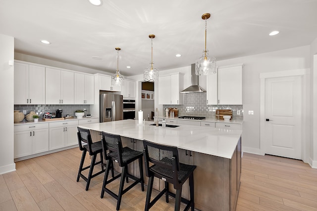 kitchen with wall chimney range hood, a spacious island, sink, appliances with stainless steel finishes, and white cabinets