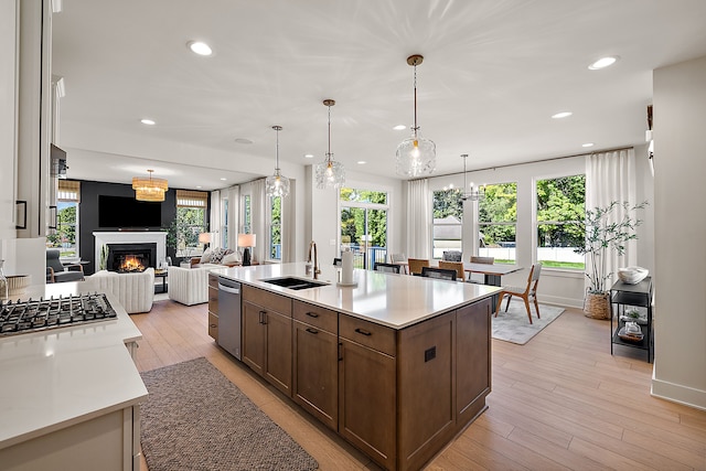 kitchen with a kitchen island with sink, dishwasher, hanging light fixtures, light hardwood / wood-style flooring, and sink