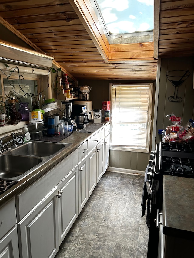 kitchen featuring wooden walls, sink, white cabinets, range, and wooden ceiling