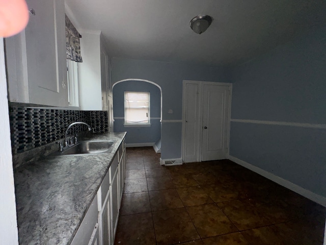 kitchen with light stone countertops, dark tile patterned flooring, white cabinets, tasteful backsplash, and sink