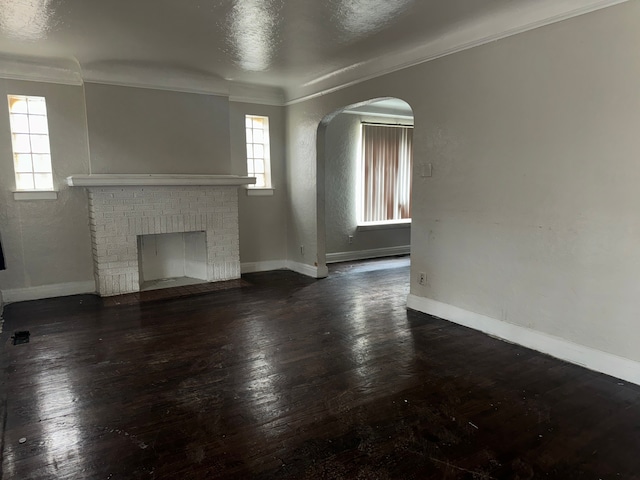 unfurnished living room with dark wood-type flooring, a brick fireplace, and ornamental molding