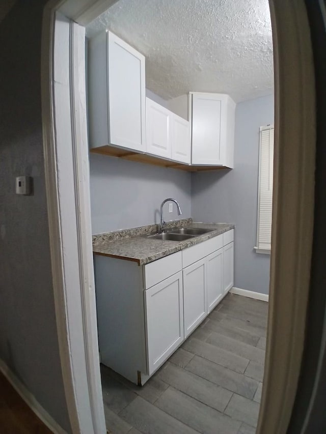 kitchen featuring sink, white cabinetry, light hardwood / wood-style floors, and a textured ceiling