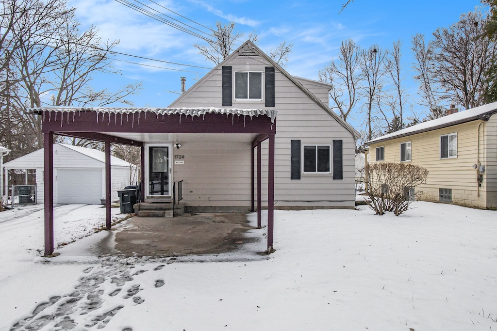 snow covered rear of property with a garage and an outbuilding