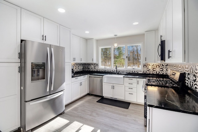 kitchen featuring pendant lighting, white cabinetry, stainless steel appliances, light hardwood / wood-style floors, and decorative backsplash