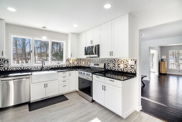 kitchen with pendant lighting, light hardwood / wood-style flooring, stainless steel appliances, and white cabinets