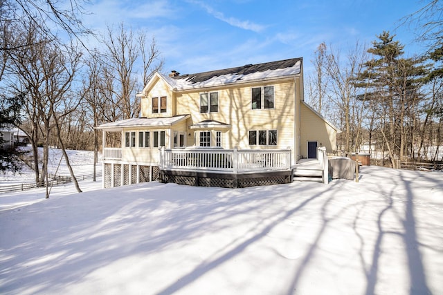 snow covered back of property with a wooden deck and a sunroom