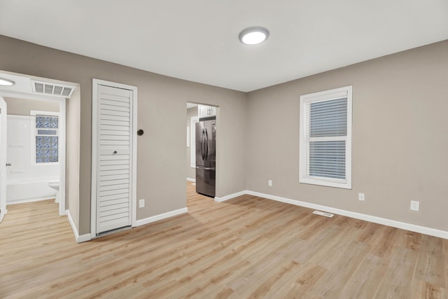 unfurnished bedroom featuring ensuite bath, a closet, stainless steel refrigerator, and light hardwood / wood-style flooring