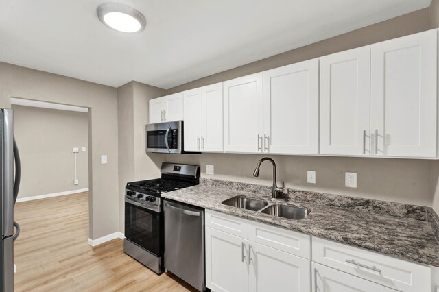 kitchen featuring appliances with stainless steel finishes, dark stone countertops, white cabinetry, and sink