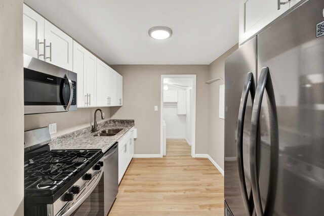 kitchen with light stone countertops, white cabinets, stainless steel appliances, sink, and light wood-type flooring