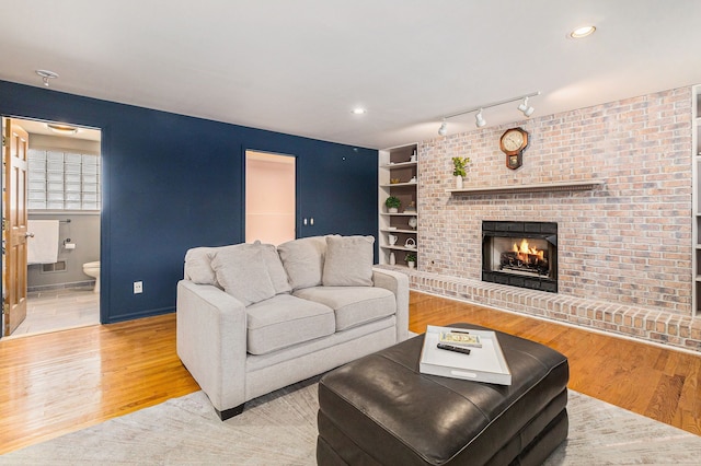 living room with rail lighting, built in features, light hardwood / wood-style floors, and a brick fireplace