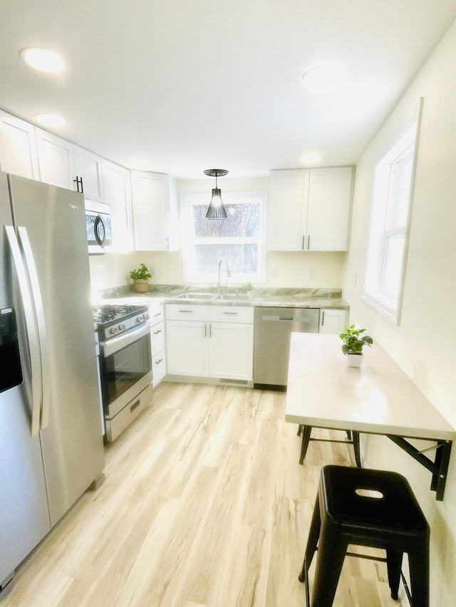 kitchen with a wealth of natural light, sink, white cabinetry, light hardwood / wood-style flooring, and appliances with stainless steel finishes