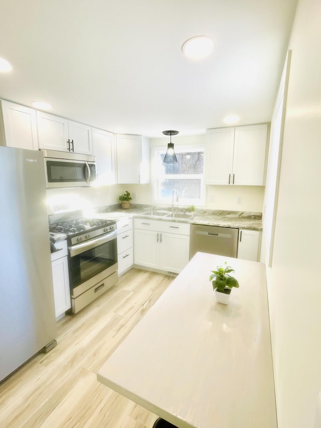 kitchen with appliances with stainless steel finishes, sink, white cabinetry, and light hardwood / wood-style floors