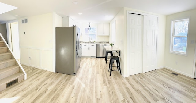 kitchen with white cabinets, appliances with stainless steel finishes, sink, light hardwood / wood-style flooring, and a breakfast bar area