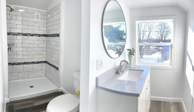 bathroom with toilet, hardwood / wood-style floors, tiled shower, vaulted ceiling, and vanity