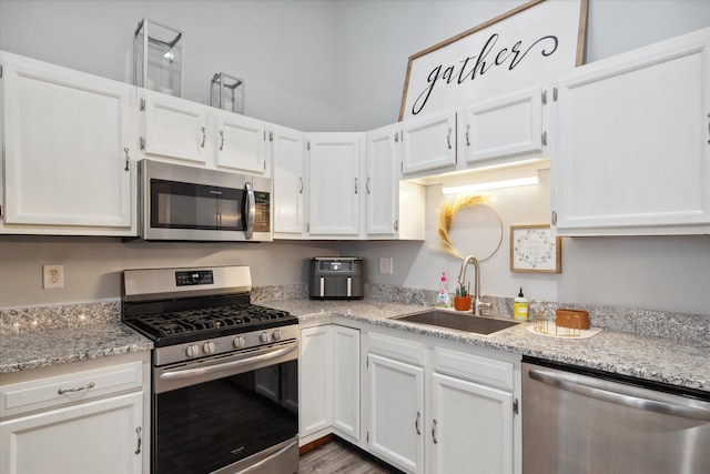 kitchen featuring stainless steel appliances, dark wood-type flooring, white cabinets, light stone counters, and sink