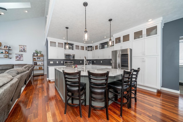 kitchen with a center island with sink, decorative backsplash, a skylight, appliances with stainless steel finishes, and light stone counters