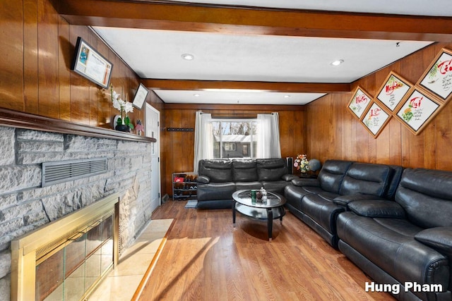 living room featuring light hardwood / wood-style flooring, a stone fireplace, beamed ceiling, and wooden walls