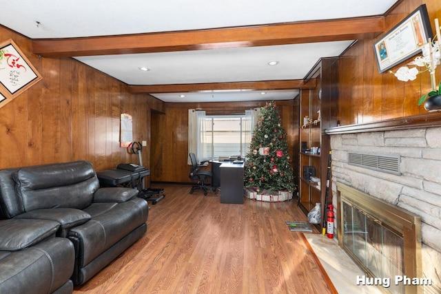 living room with a stone fireplace, beam ceiling, hardwood / wood-style floors, and wooden walls