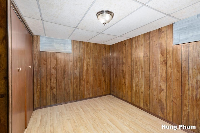 basement featuring light wood-type flooring, a paneled ceiling, and wooden walls