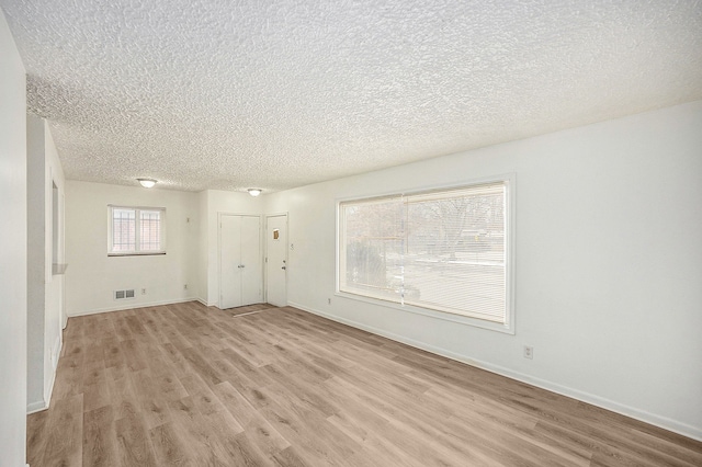 unfurnished living room featuring light wood-type flooring, a textured ceiling, and a healthy amount of sunlight