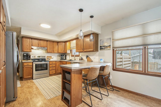 kitchen featuring pendant lighting, appliances with stainless steel finishes, kitchen peninsula, a breakfast bar, and light hardwood / wood-style flooring