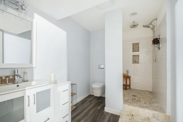 bathroom featuring hardwood / wood-style flooring, toilet, vanity, and a tile shower