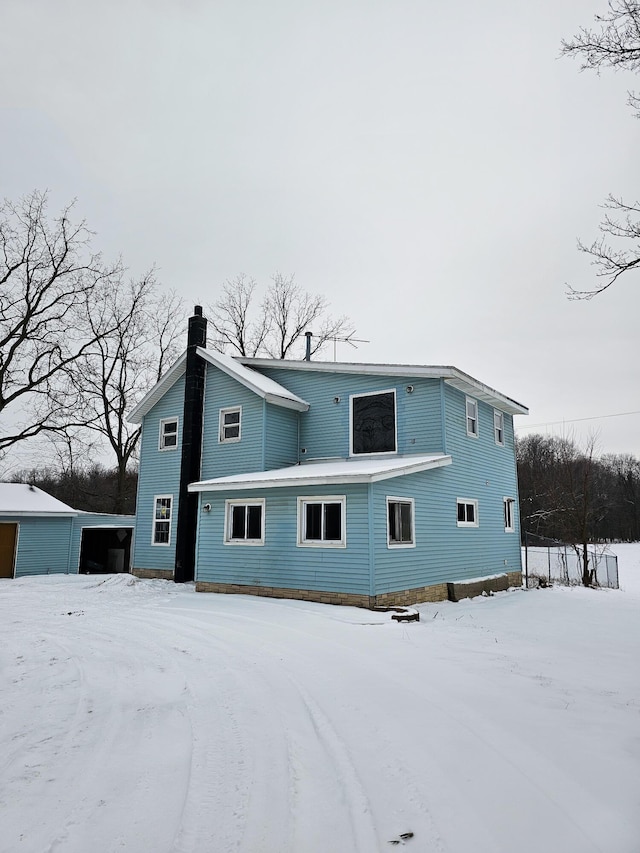 snow covered property featuring a chimney and a detached garage