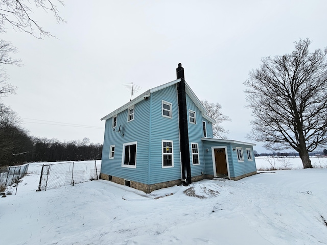 snow covered property featuring a chimney and fence
