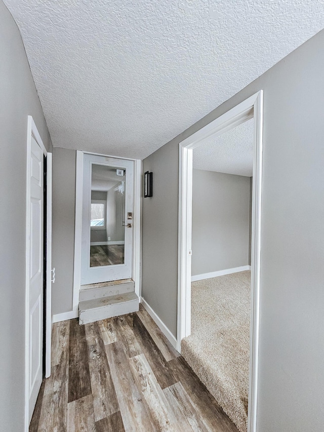 hall with a textured ceiling, wood finished floors, and baseboards