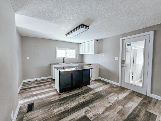 kitchen with a sink, wood finished floors, white cabinetry, a textured ceiling, and baseboards