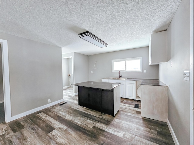 kitchen with a sink, white cabinets, a center island, wood finished floors, and a textured ceiling