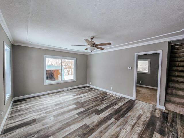 spare room with ornamental molding, a textured ceiling, wood finished floors, a ceiling fan, and baseboards