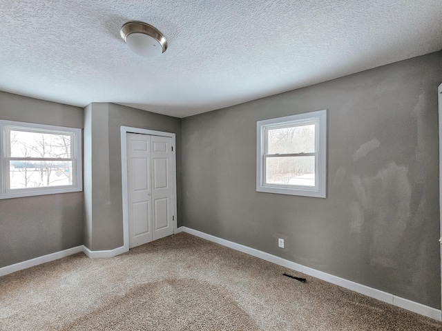 unfurnished bedroom with multiple windows, a closet, baseboards, carpet floors, and a textured ceiling