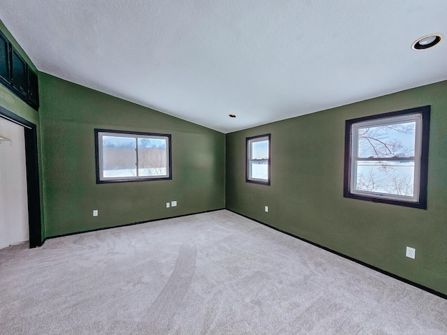 carpeted spare room with vaulted ceiling, baseboards, and a textured ceiling