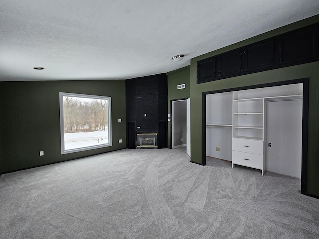 unfurnished bedroom featuring light colored carpet, a large fireplace, a textured ceiling, and lofted ceiling
