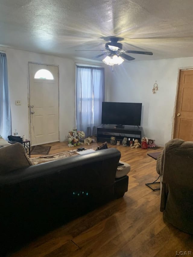 living room with a textured ceiling, dark wood-type flooring, and ceiling fan