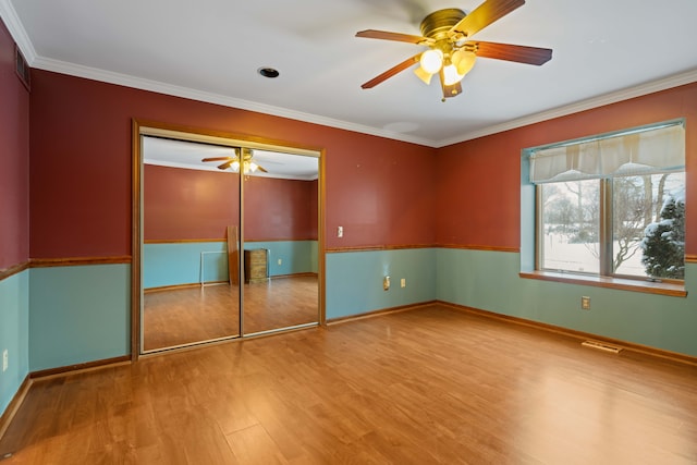 unfurnished bedroom with crown molding, ceiling fan, a closet, and hardwood / wood-style flooring