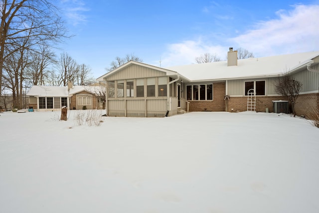 snow covered rear of property with central AC unit and a sunroom