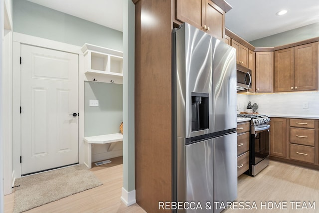 kitchen with appliances with stainless steel finishes, light hardwood / wood-style flooring, and decorative backsplash