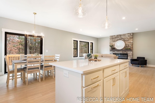 kitchen featuring a kitchen island, a fireplace, hanging light fixtures, a notable chandelier, and light hardwood / wood-style floors