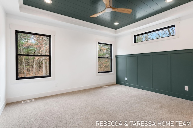 empty room with ceiling fan, carpet flooring, a tray ceiling, and wooden ceiling