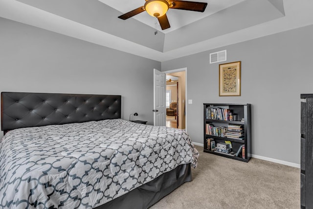 bedroom with ceiling fan, light colored carpet, and a tray ceiling