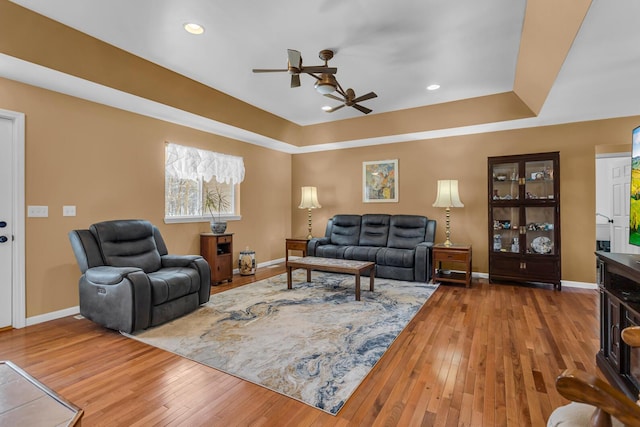 living room featuring ceiling fan, hardwood / wood-style flooring, and a tray ceiling