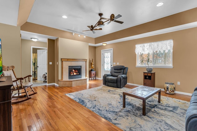 living room with ceiling fan, hardwood / wood-style floors, track lighting, and a tiled fireplace