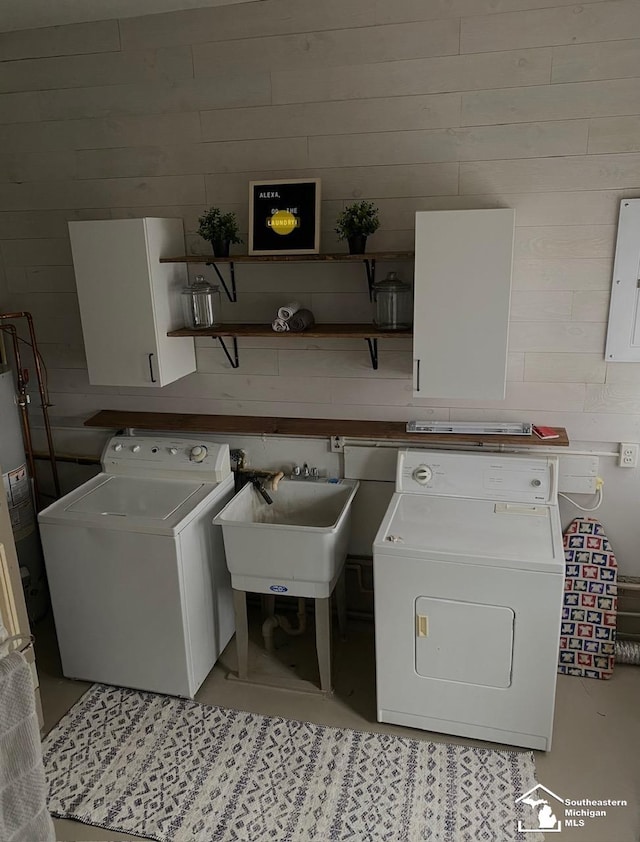 laundry area with wooden walls, independent washer and dryer, cabinets, electric panel, and sink