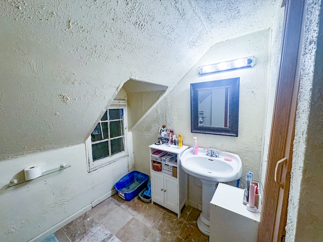 bathroom featuring vaulted ceiling, sink, and a textured ceiling